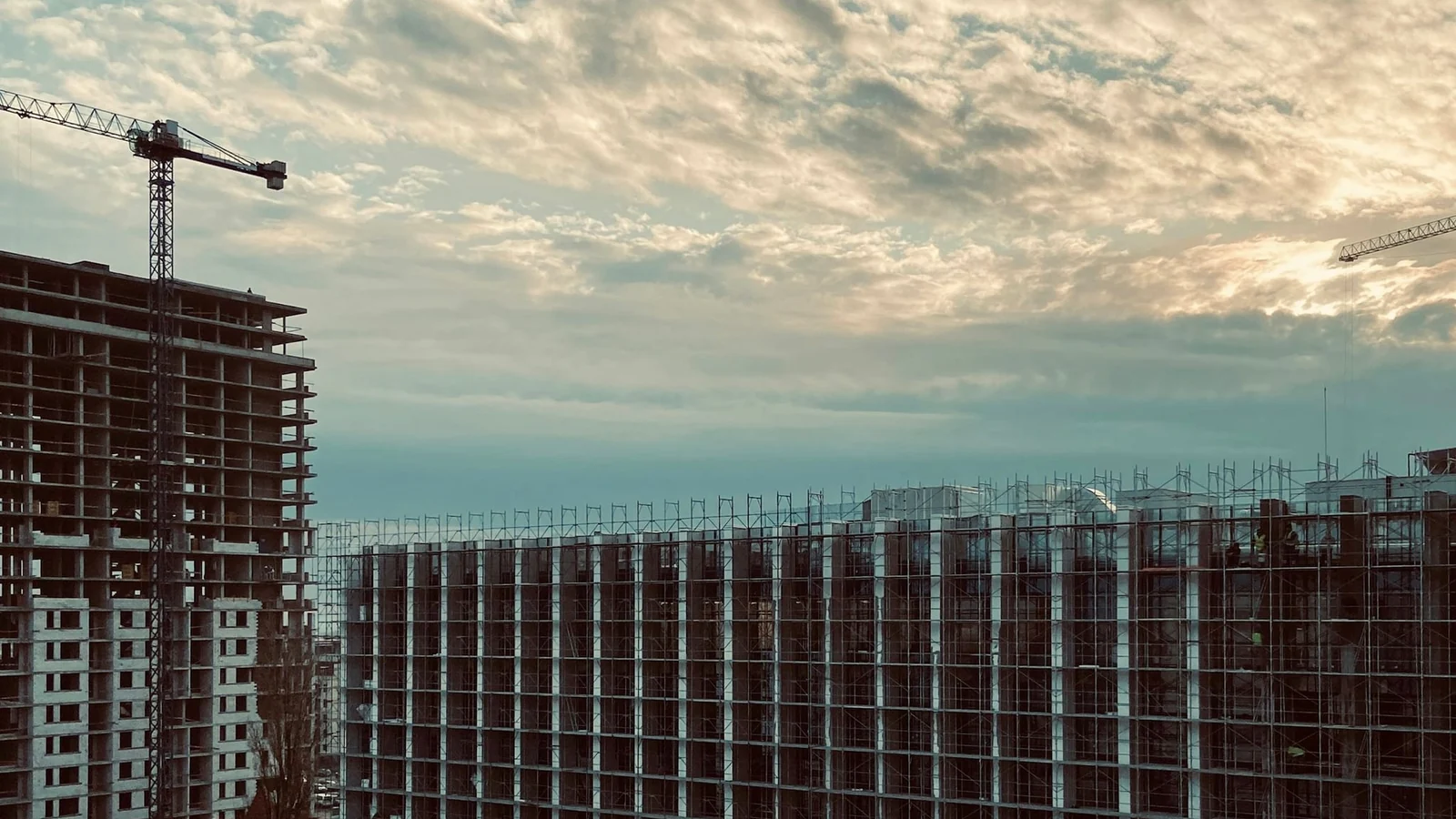 Cranes and the structure of a building under construction at dusk.